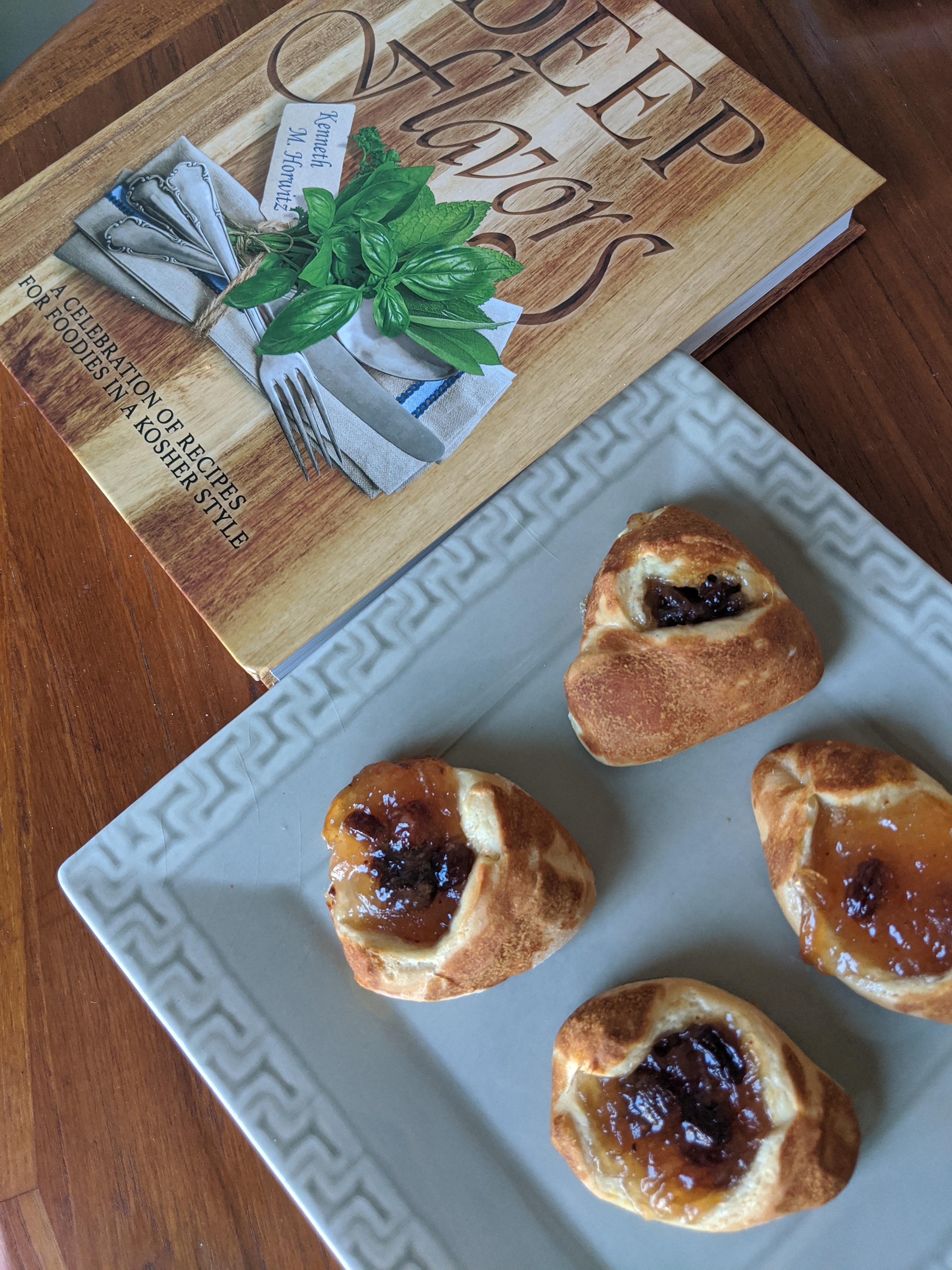 Four dark Hamantaschen next to the "Deep Flavors" cookbook