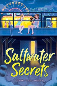 Cover of Saltwater Secrets by Cindy Callaghan. Yellow text on a mostly blue-hued image of two girls sitting on a boardwalk. There are people standing in the near background, and a ferris wheel and roller coaster stand in the distance.